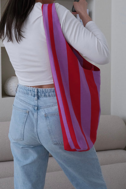 Person holding a red and pink striped bag in a living room setting