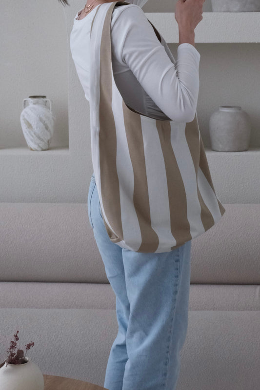 Person wearing a striped shirt and light blue jeans in a minimalistic room with white walls and shelves.