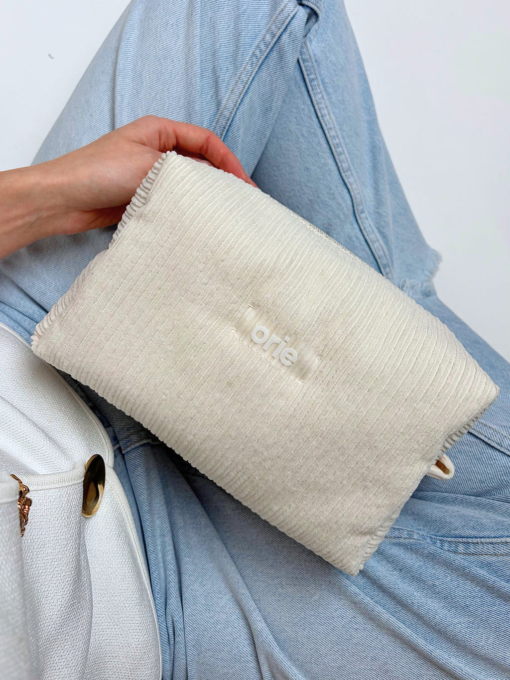 Person holding a textured beige makeuo bag  bag with 'orie' branding against a white background