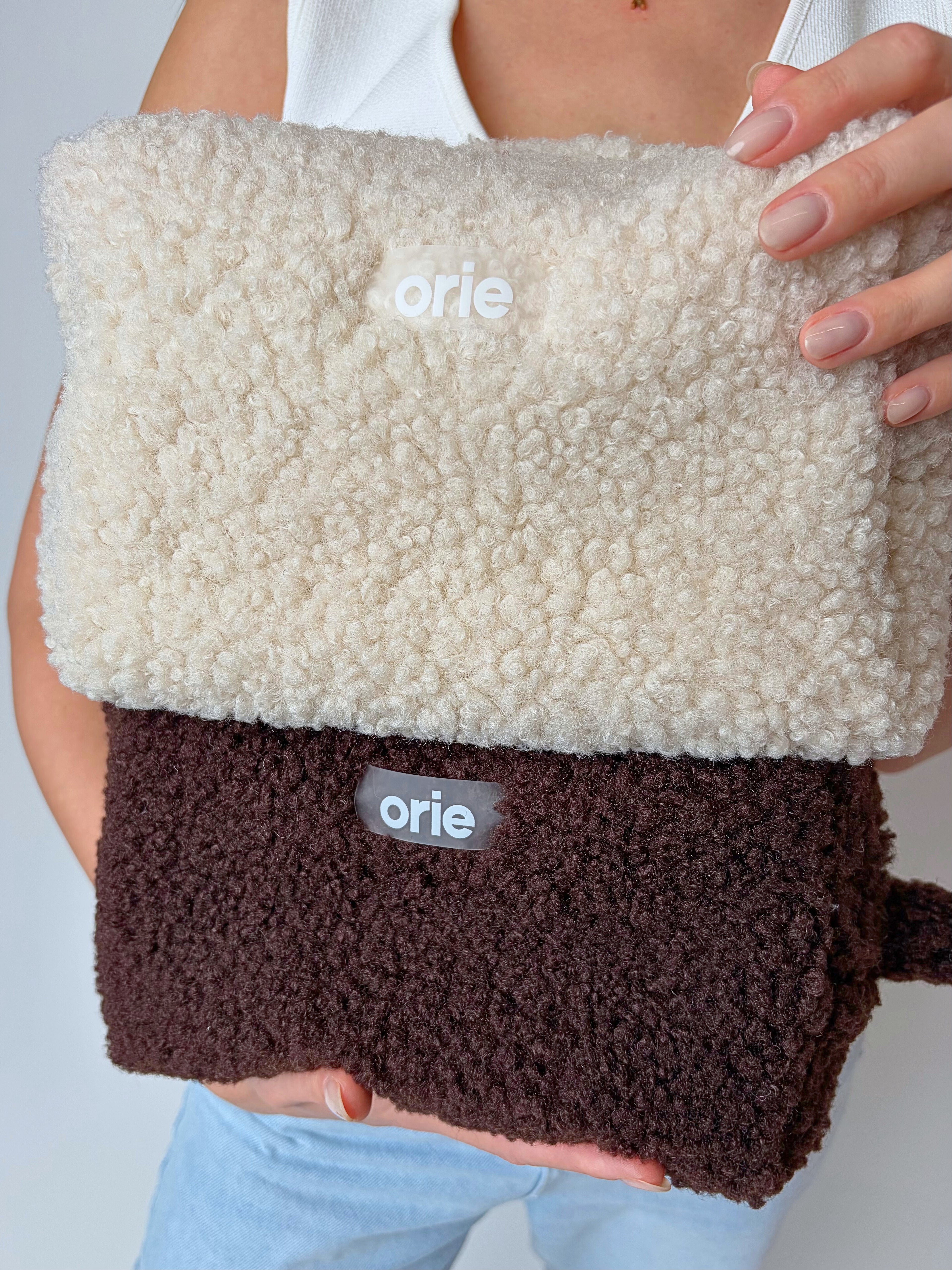 Two layered makeup bag with 'orie' branding held by a person against a neutral background
