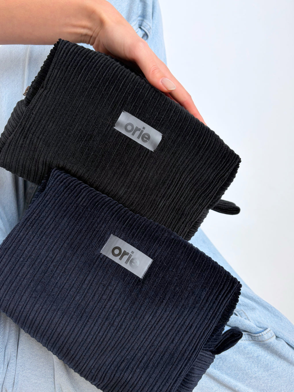 Two pairs of makeup bags with 'orie' branding held by a person against a light background.