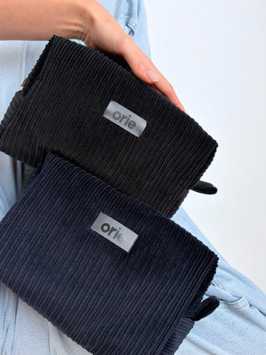 Two pairs of makeup bags with 'orie' branding held by a person against a light background.