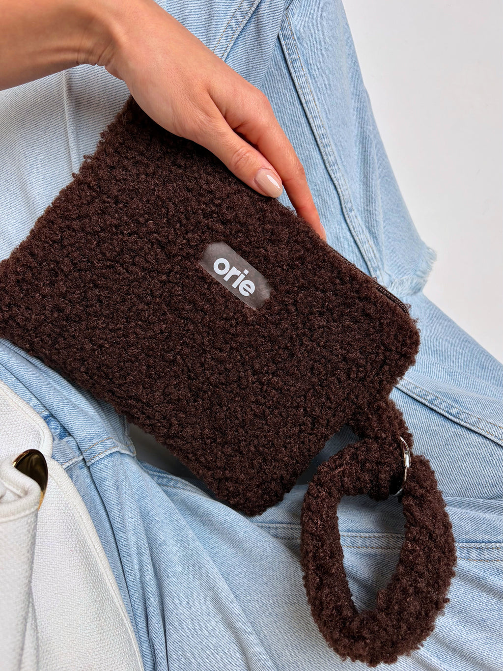Brown teddy pouch held by a person wearing a blue denim jacket.