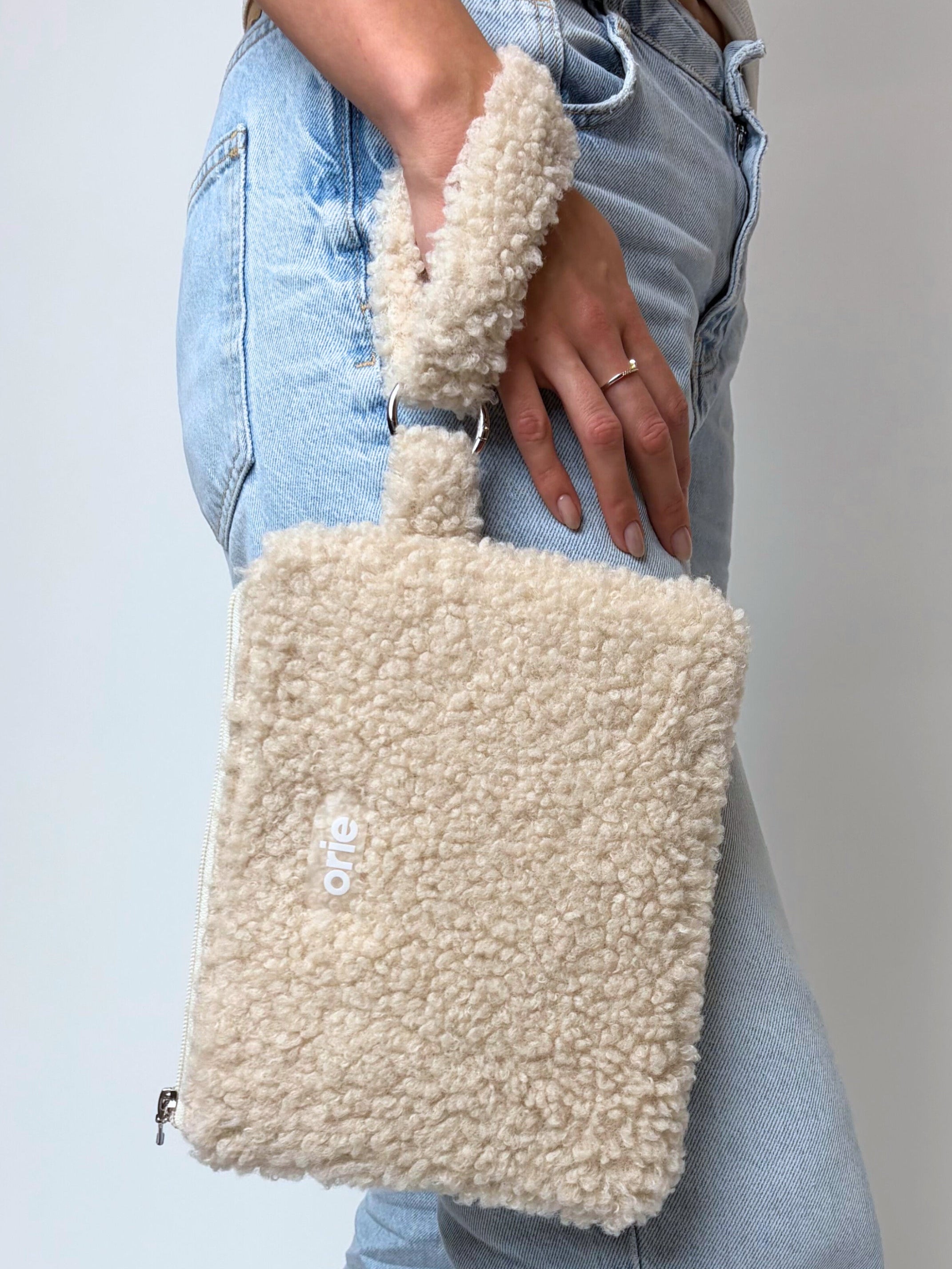Beige teddy bag held by a person wearing light blue jeans on a plain background