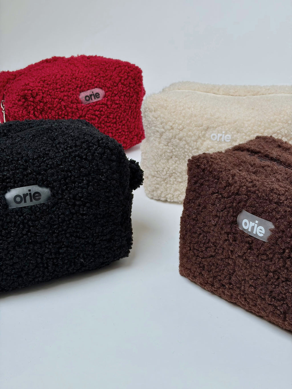 Four teddy pouches in red, black, beige, and brown with 'orie' branding on a white background.