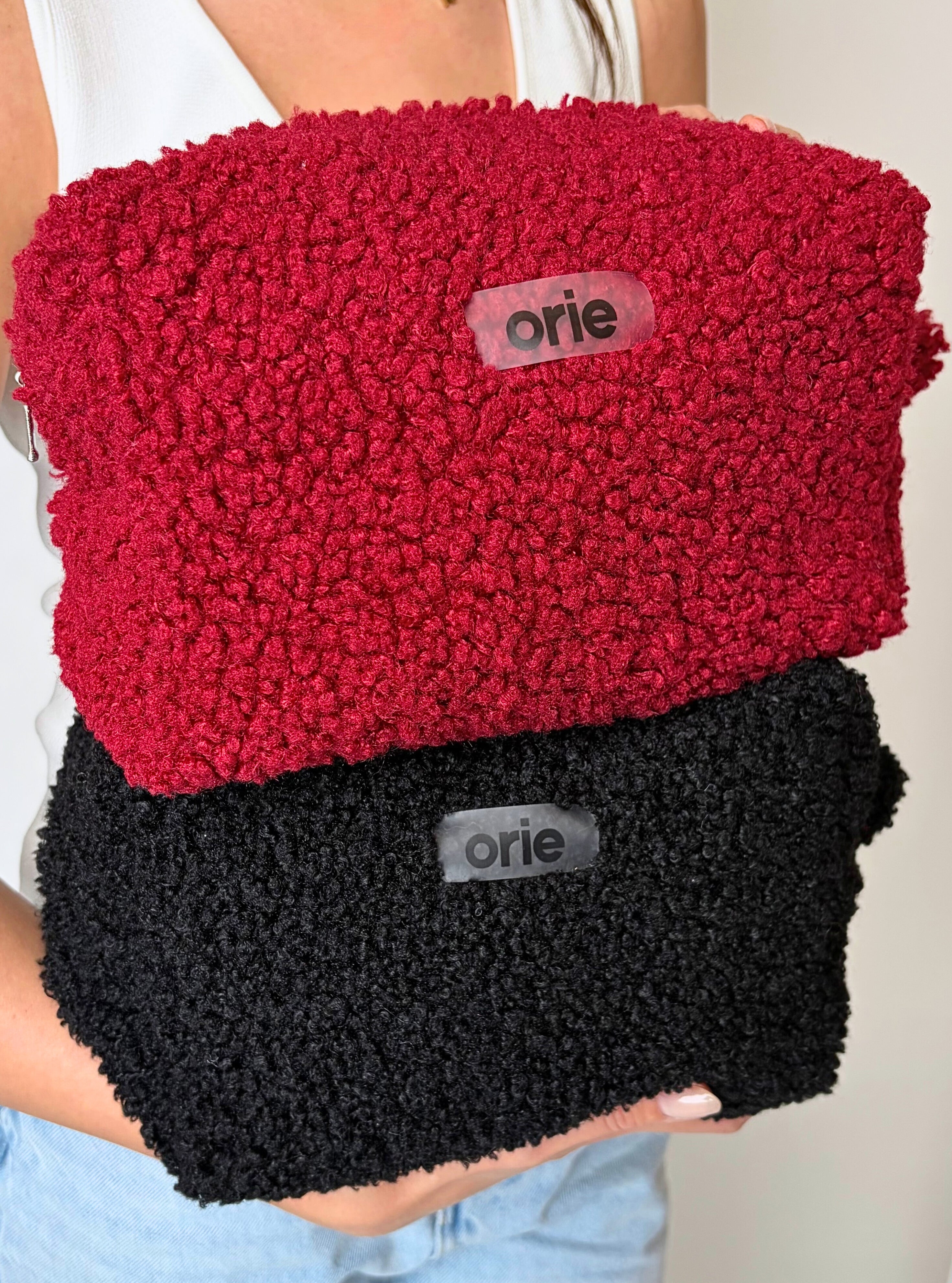 Red and black textured makeup bag held by a person, with 'orie' branding.