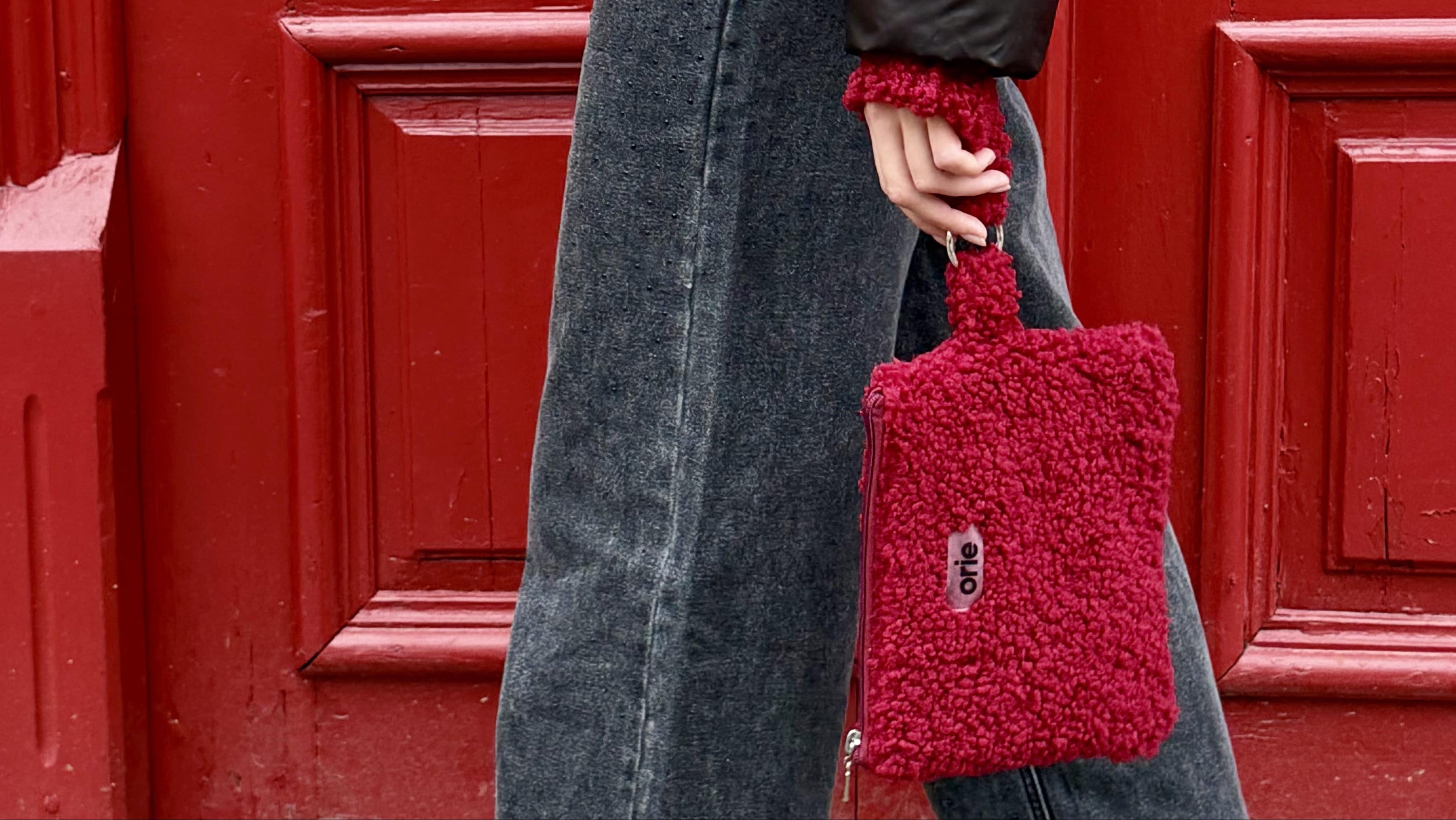 Person holding a red textured bag in front of a red door