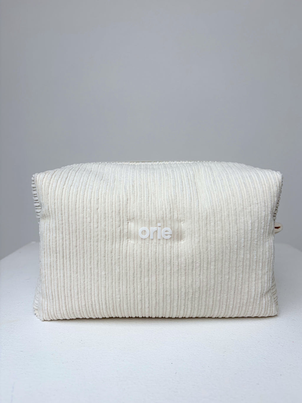 Textured velvet white makeuo bag on a gray background with 'orie' branding.
