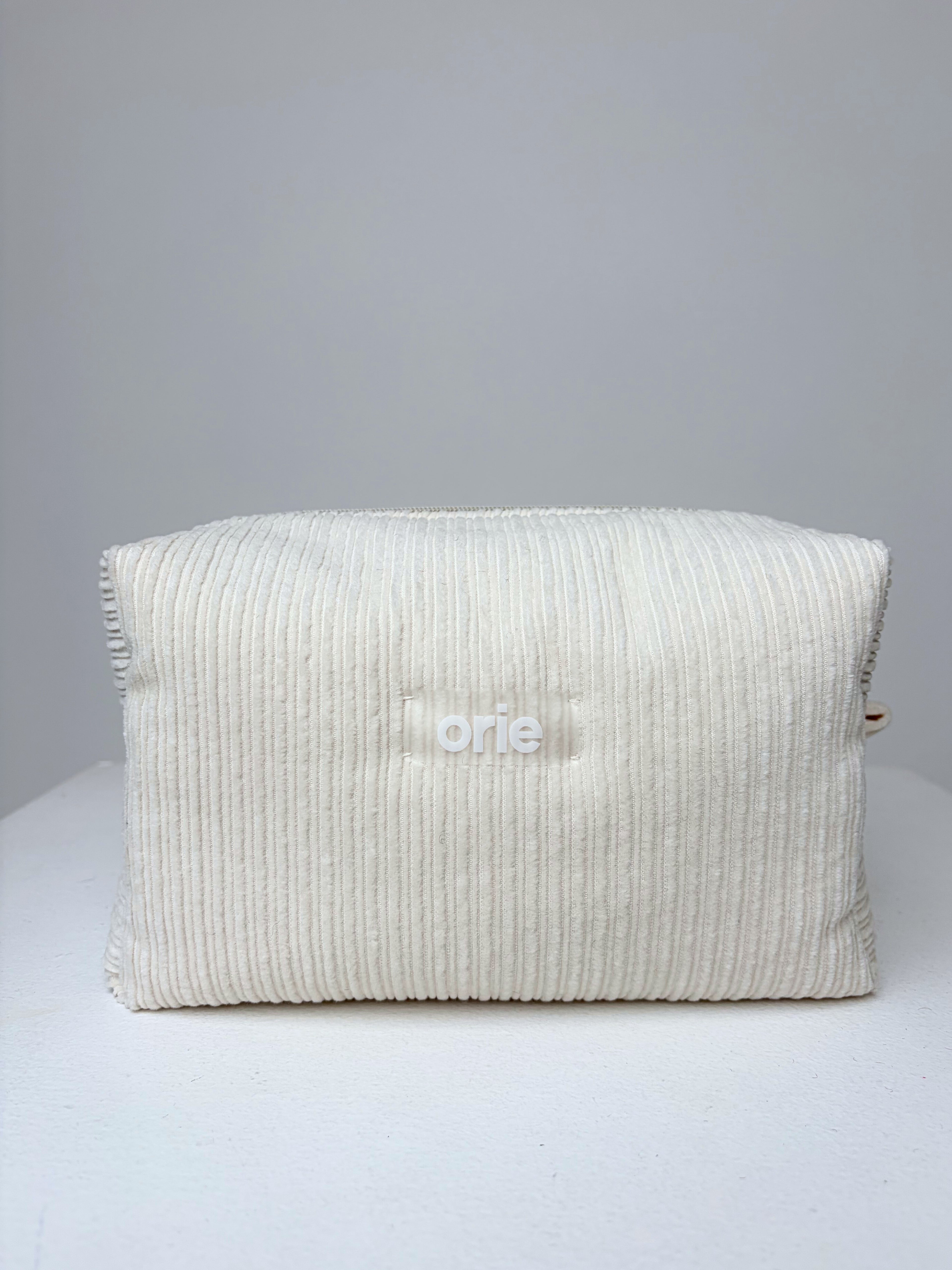 Textured velvet white makeuo bag on a gray background with 'orie' branding.