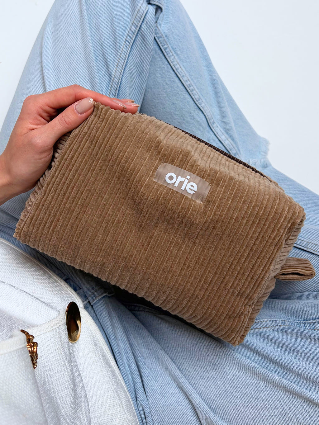 Brown makeug bag pouch held by a person with 'orie' branding on a light blue background