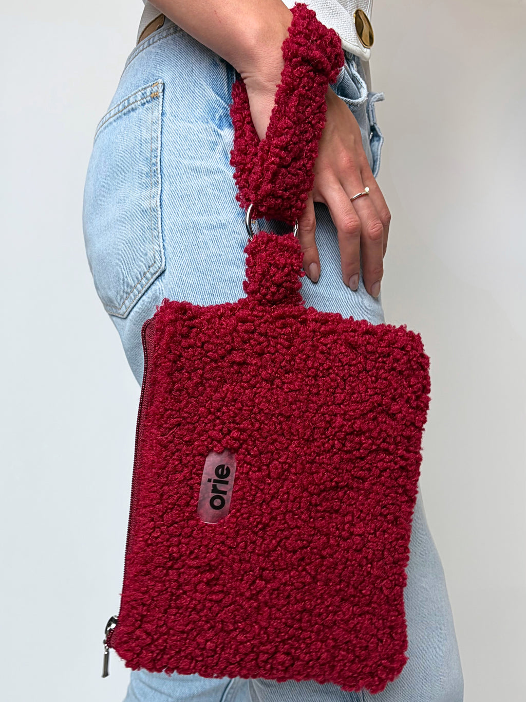Red teddy bag held by a person wearing light blue jeans against a plain background