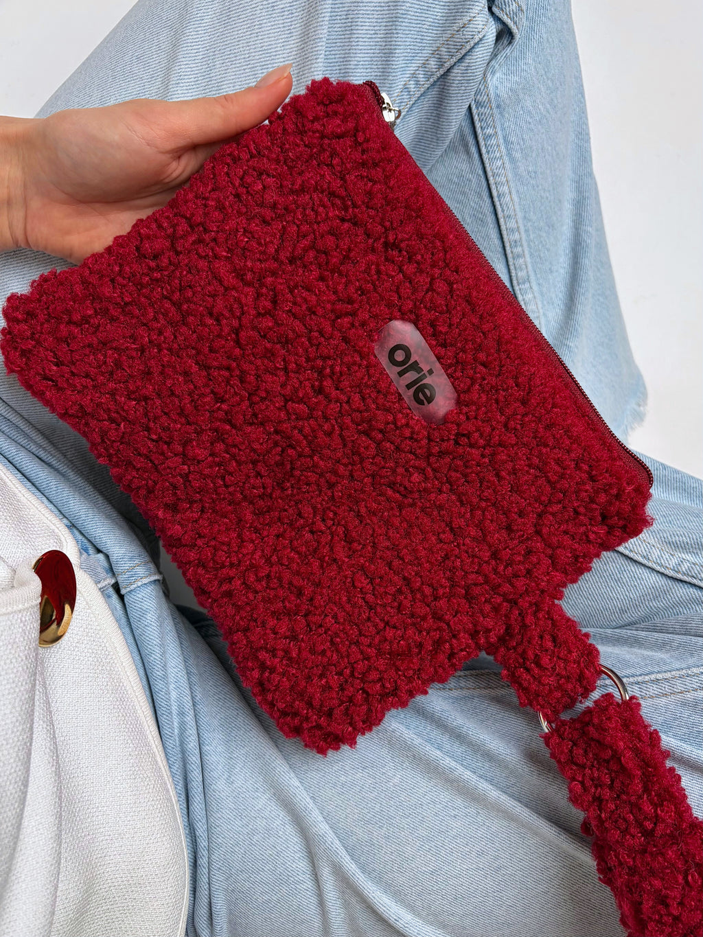 Red teddy pouch with a visible brand label held by a person wearing a light blue denim jacket.