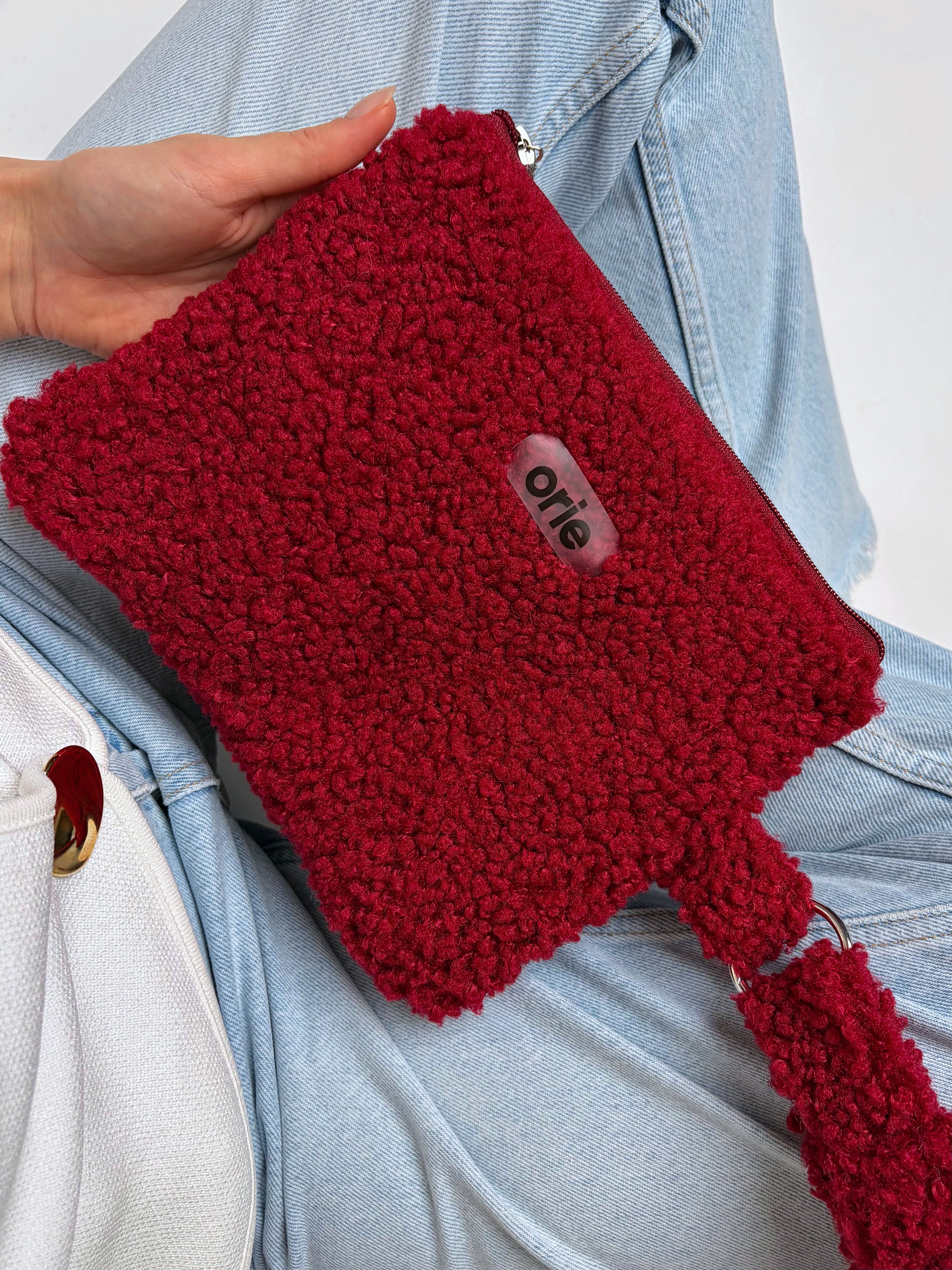 Red teddy pouch with a visible brand label held by a person wearing a light blue denim jacket.