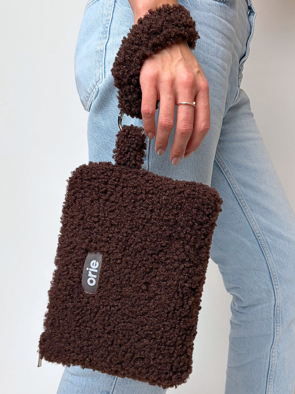 Brown tedyy handbag held by a person wearing light blue jeans on a plain background