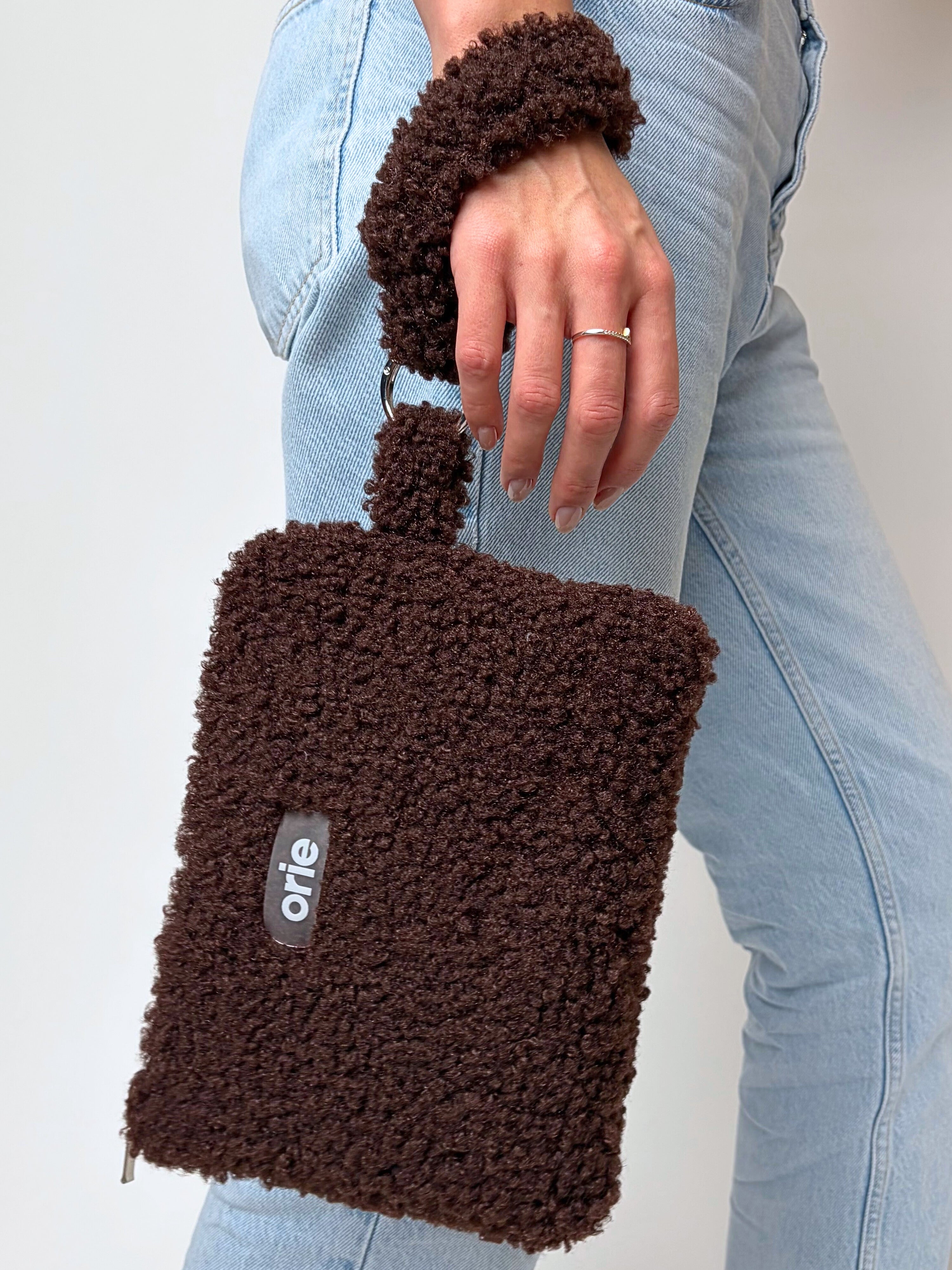 Brown tedyy handbag held by a person wearing light blue jeans on a plain background