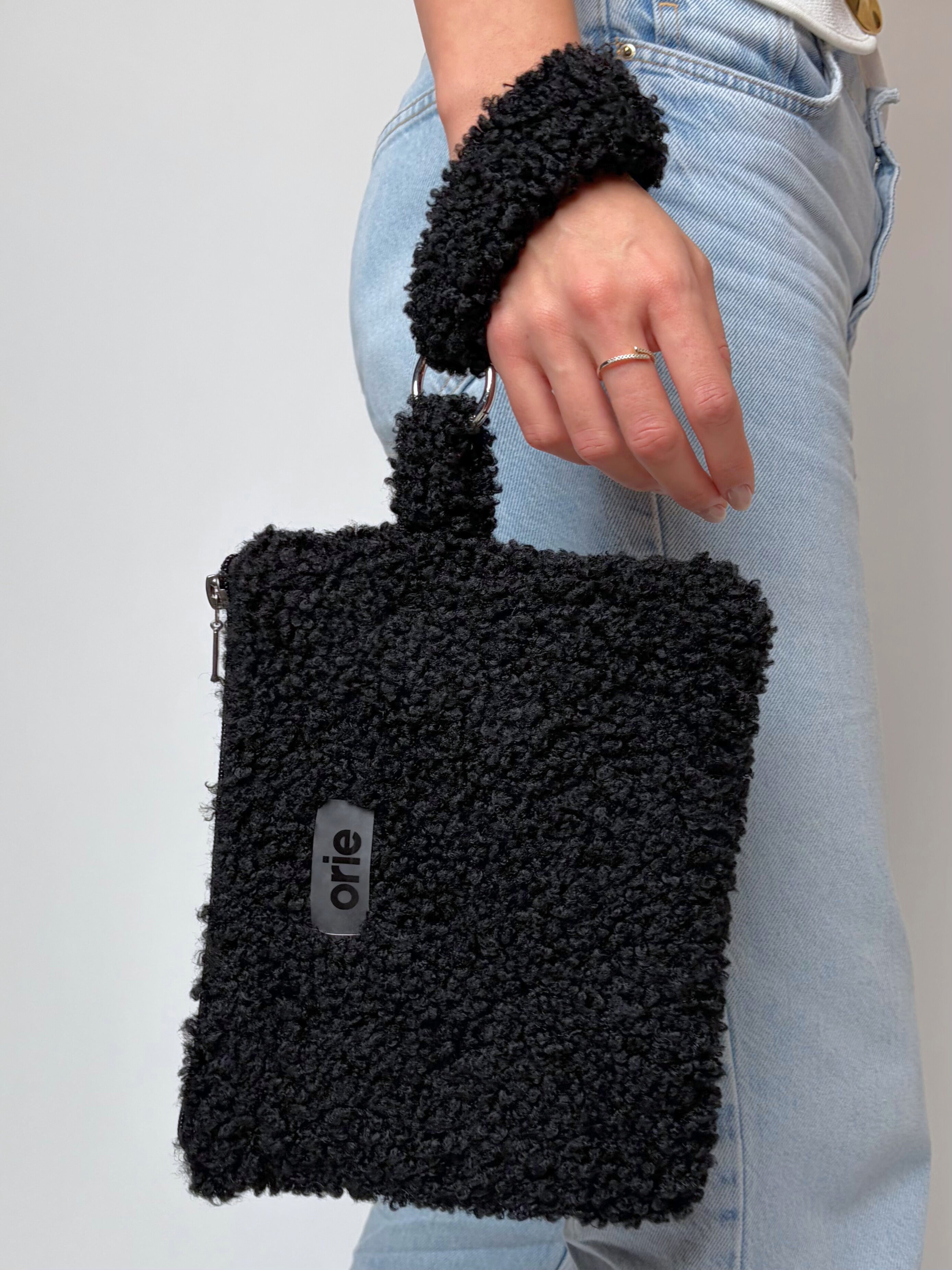 Black teddy handbag held by a person wearing light blue jeans on a gray background