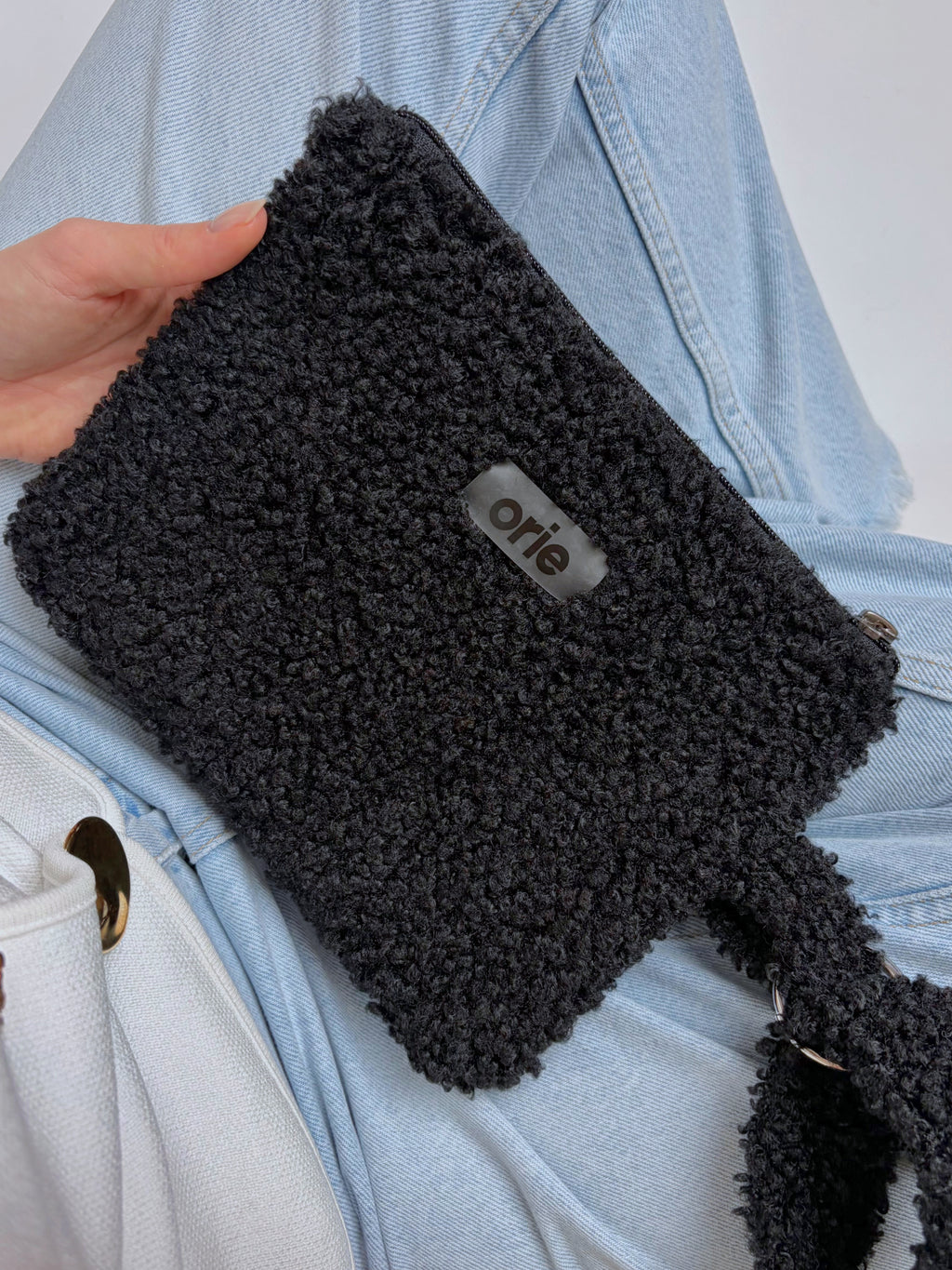 Black teddy pouch held by a person with a visible brand logo against a light blue denim background.