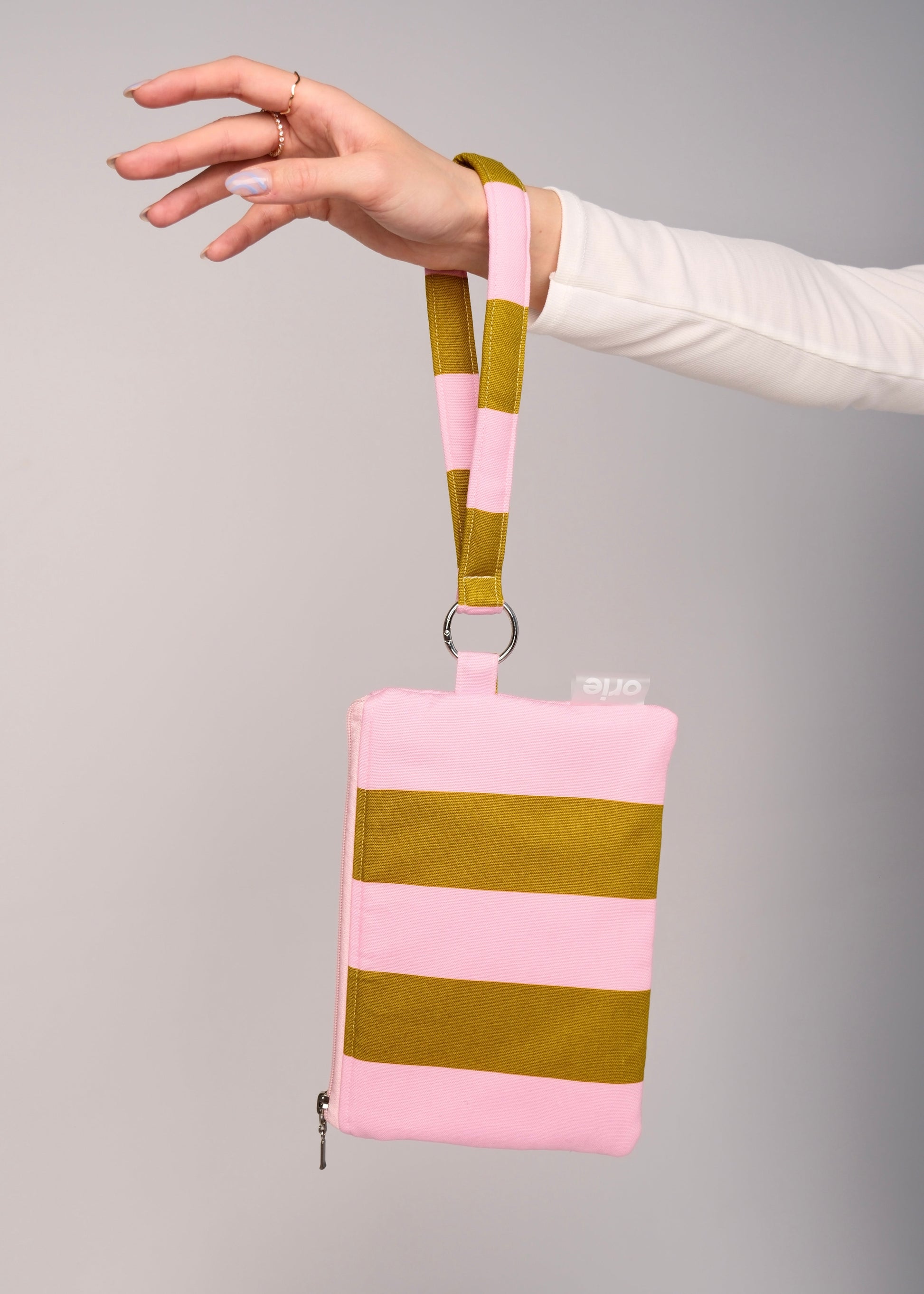 Hand holding a pink and green striped pouch against a gray background orie brand
