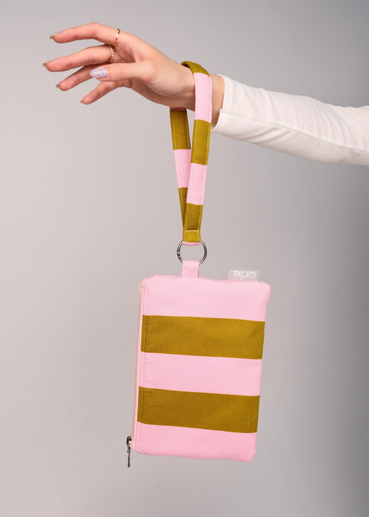 Hand holding a pink and green striped pouch against a gray background orie brand