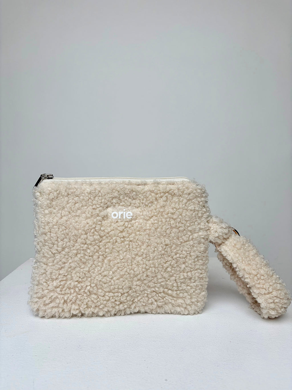 Beige teddy pouch with a visible brand logo on a light gray background