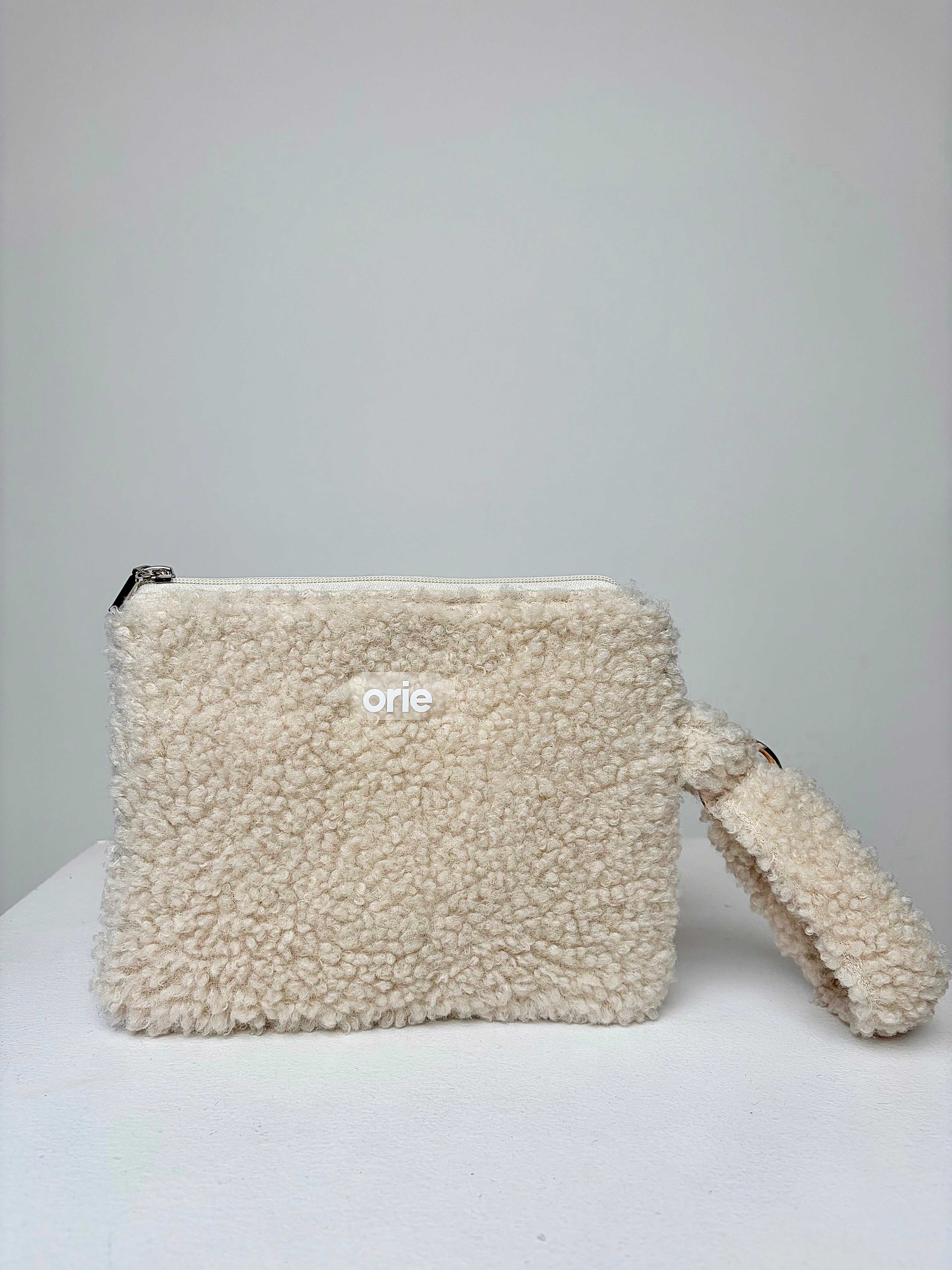 Beige teddy pouch with a visible brand logo on a light gray background