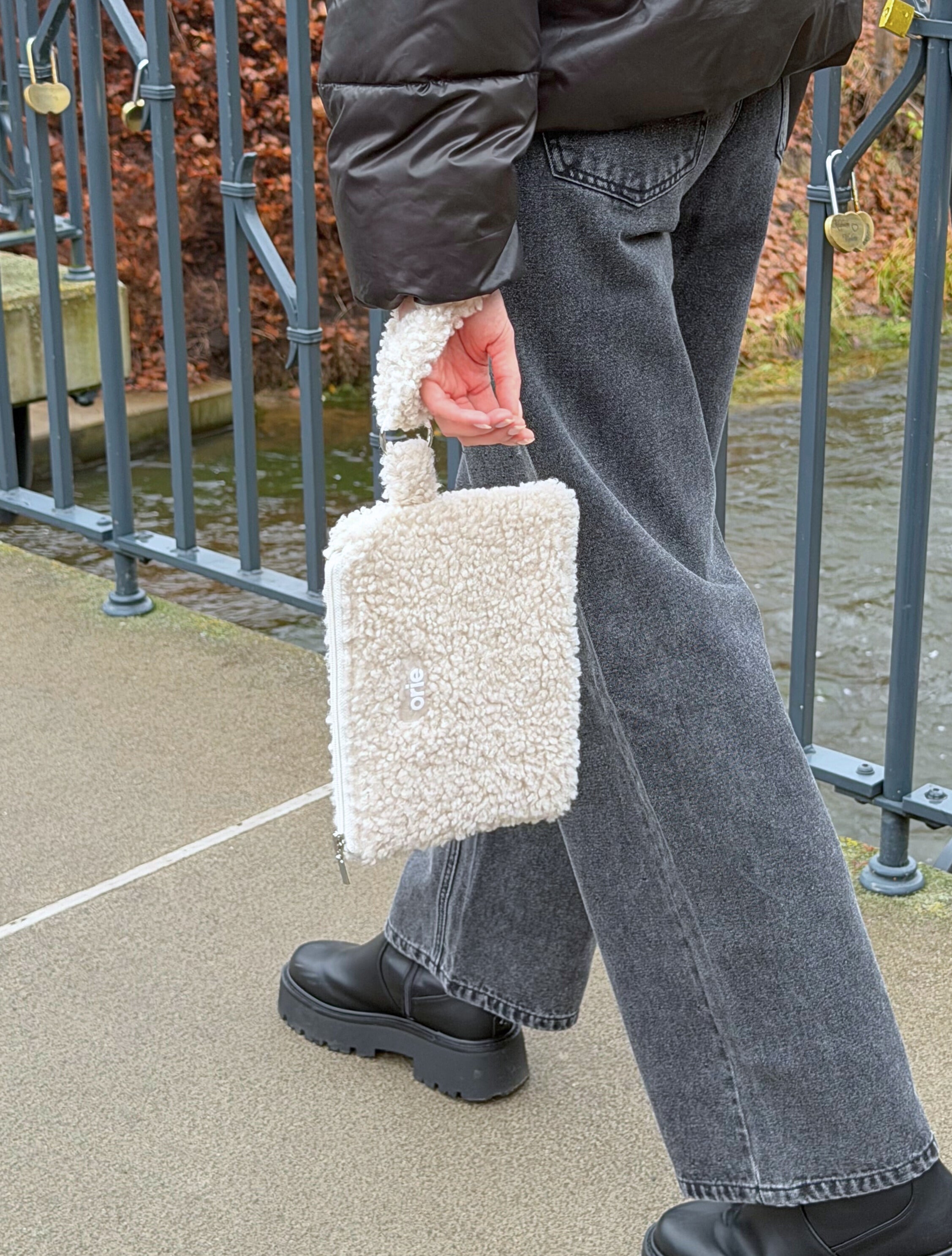 Person holding a fluffy teddy white handbag outdoors near a metal gate.