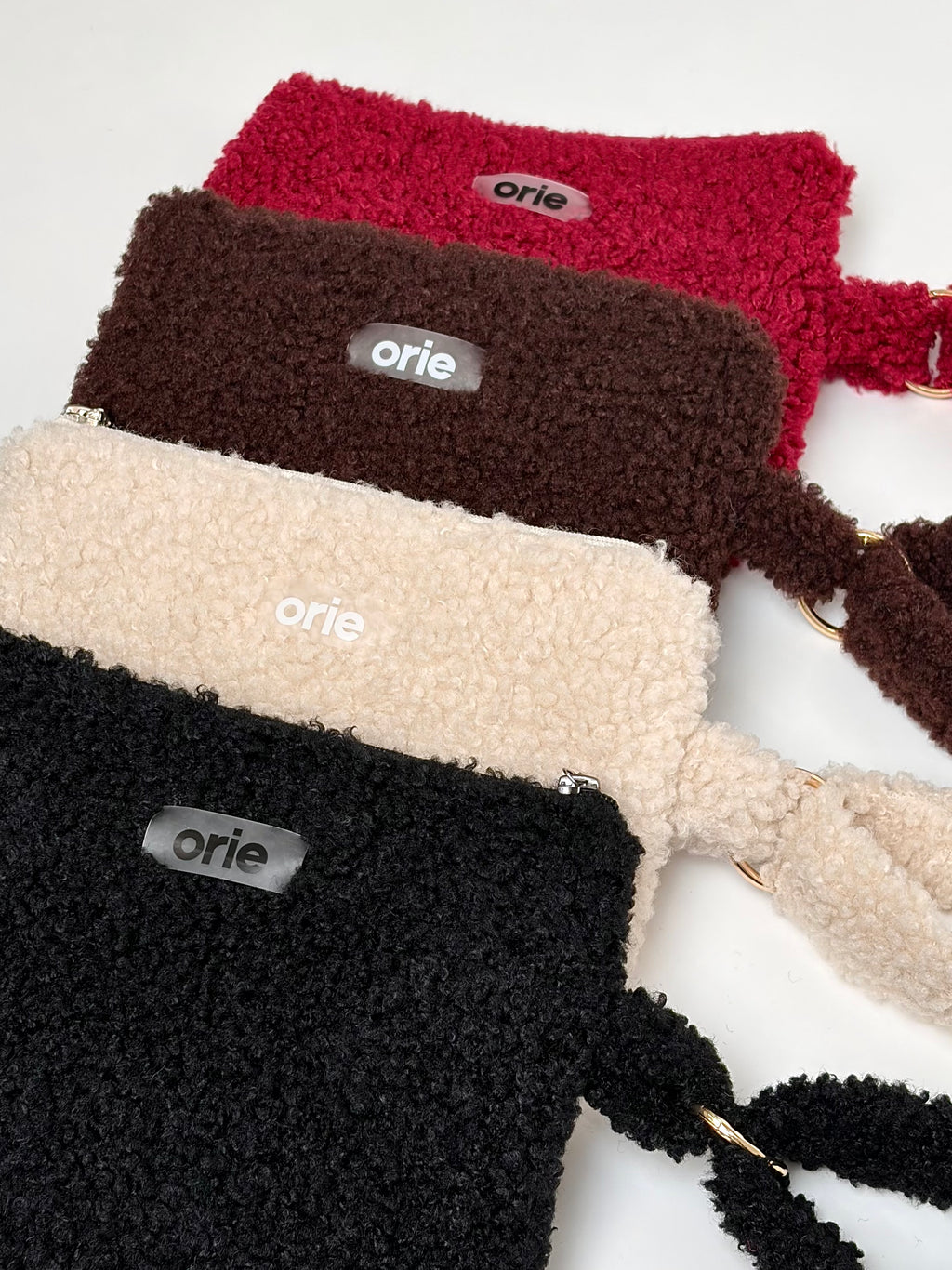 Four teddy-lined pouches in black, brown, red, and beige with 'orie' branding on a white background.