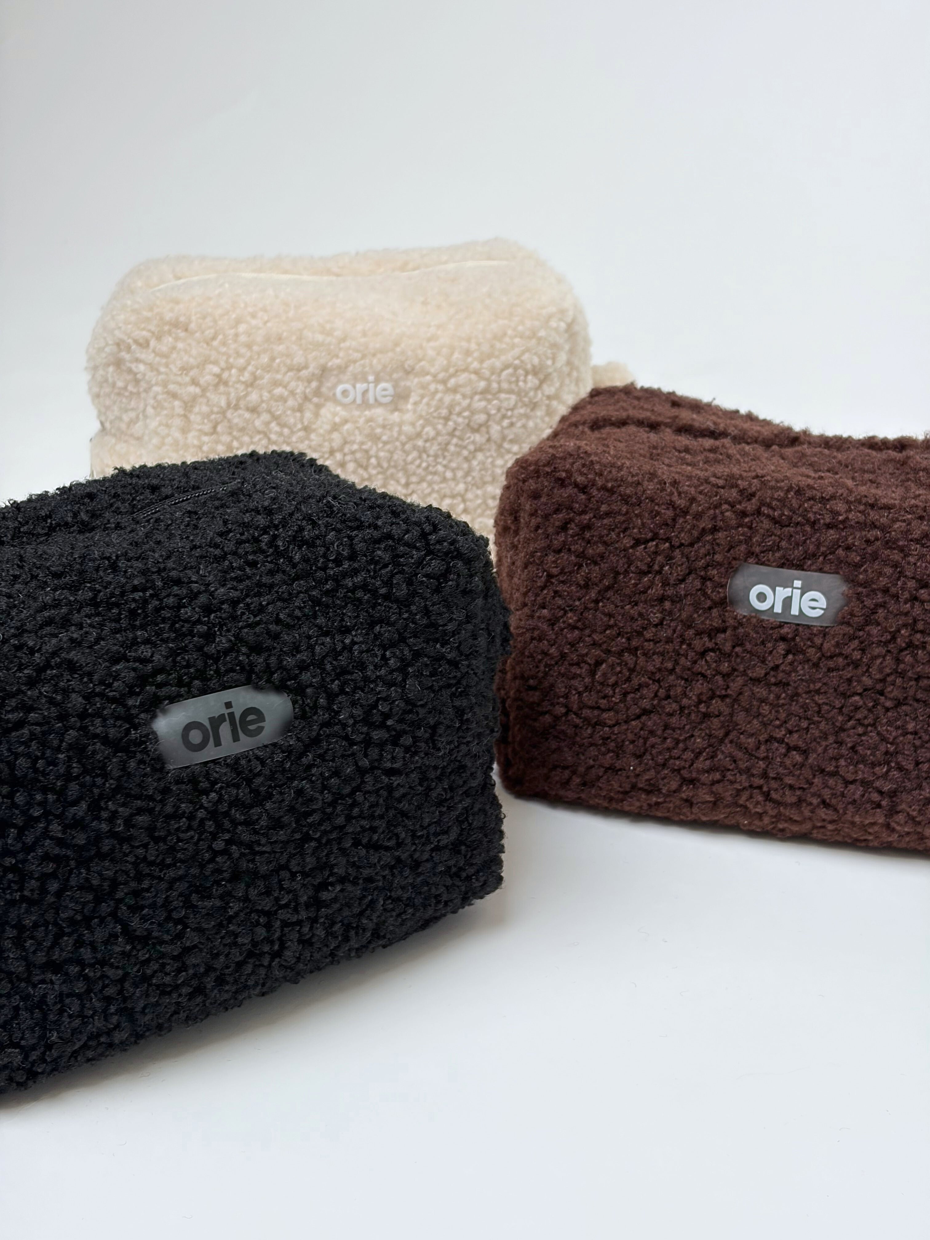 Four plush makeup bags in beige, black, and brown with 'orie' branding on a white background
